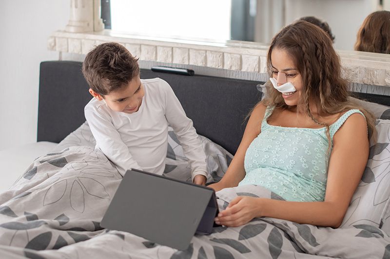 Woman spending time with child in bed after rhinoplasty surgery.